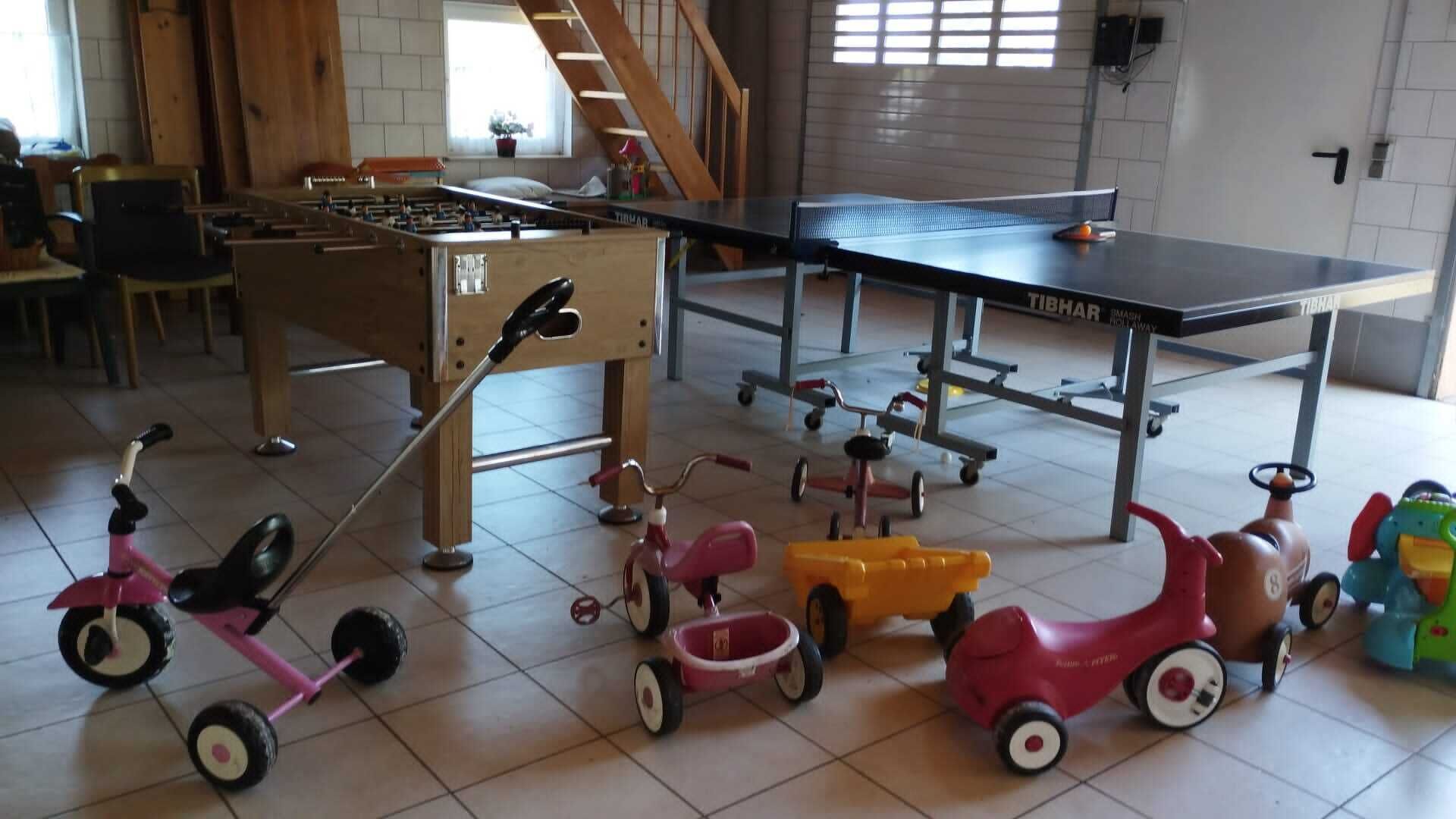 A spacious indoor area with a ping pong table, a foosball table, and various children's toys.