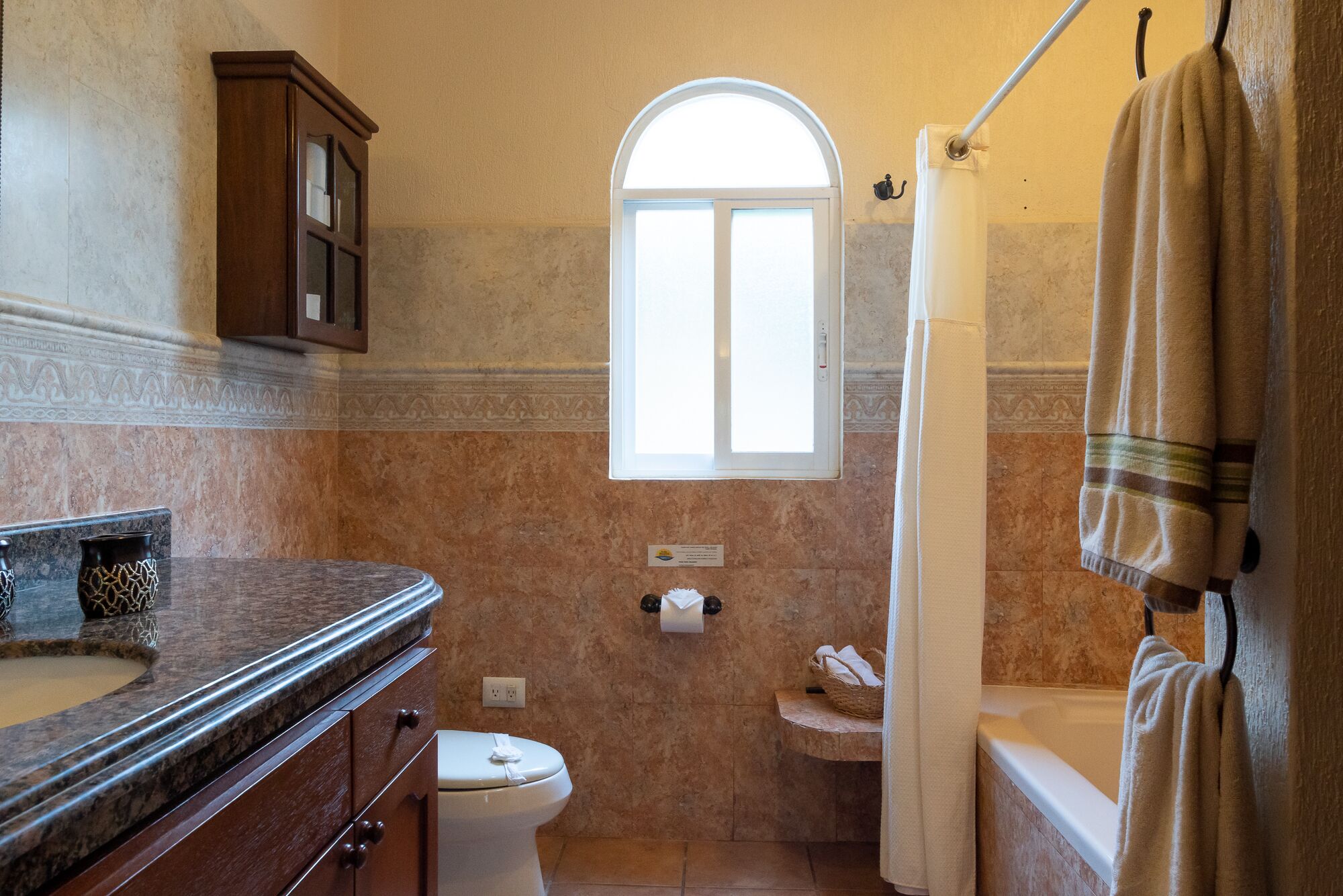 Une salle de bain avec un lavabo en marbre, des toilettes, une baignoire et une fenêtre.
