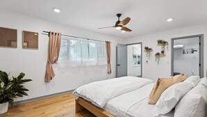 A modern bedroom with a wooden bed, a ceiling fan, and a large window with curtains. - Luxury Oasis w/ Private Pool - 5-Minutes to Beach (Seminole)