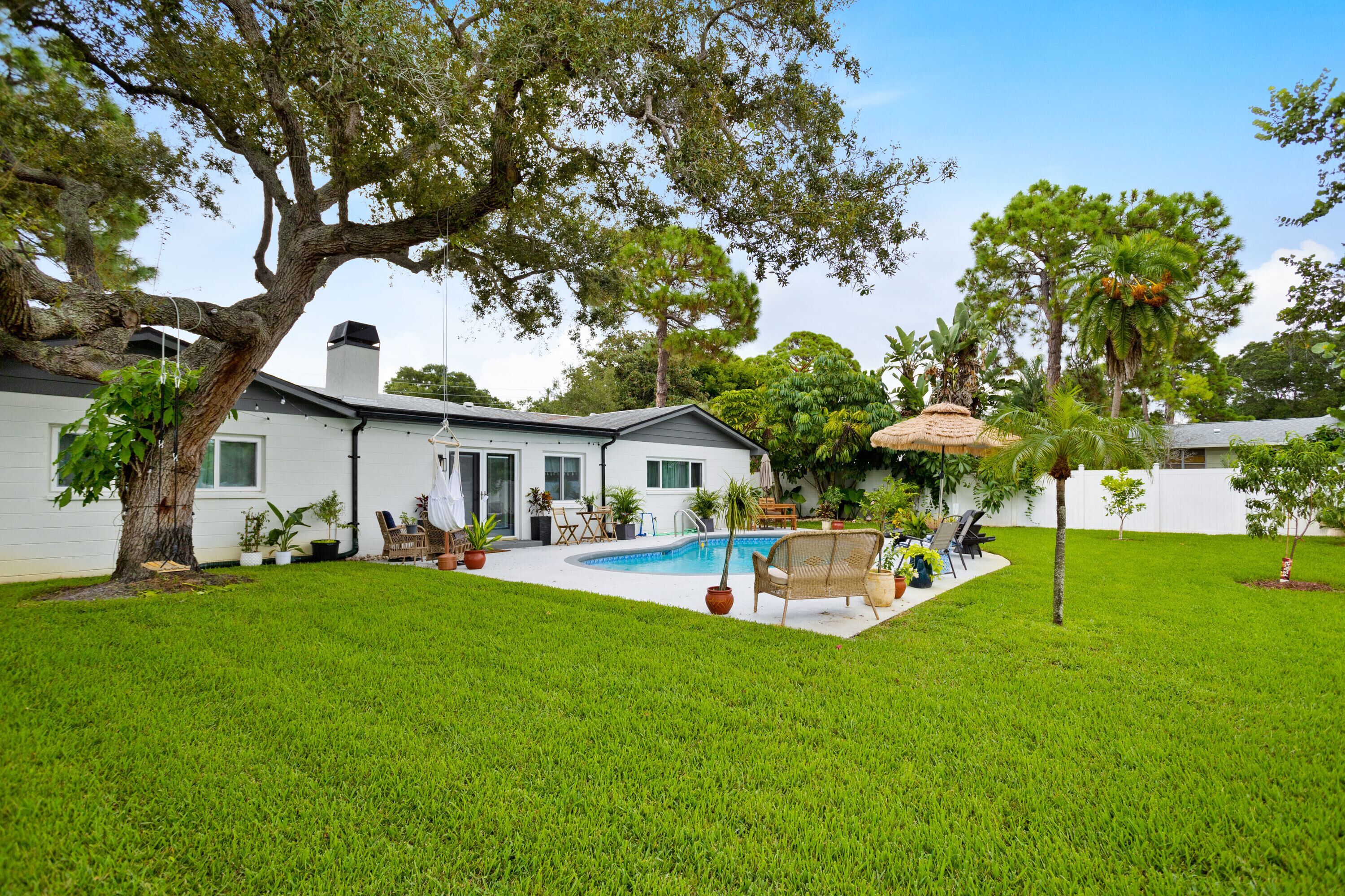 A backyard with a swimming pool, a dining area, and a large tree.