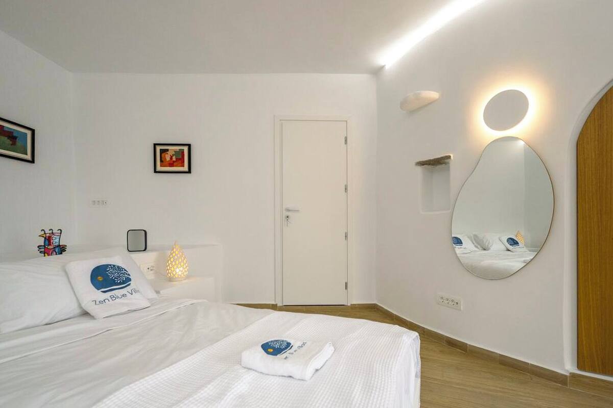 A hotel room with a bed, a bedside table with a lamp, a mirror, and a door.