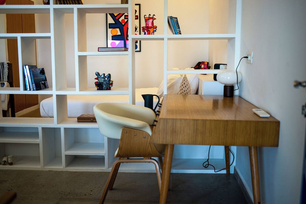 A modern room with a wooden desk, a white chair, and a bookshelf filled with books and decorative items.