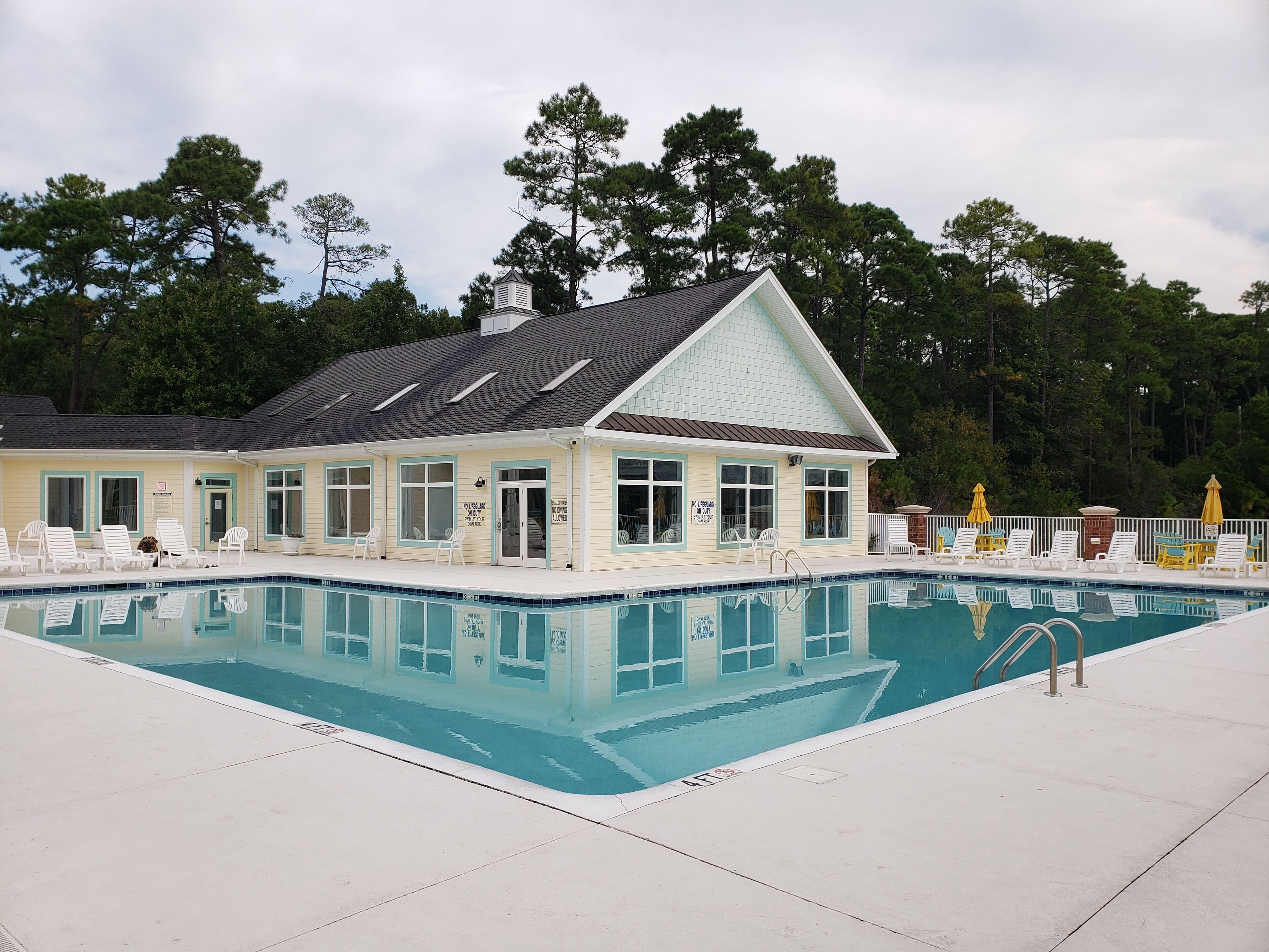 Un bâtiment situé au bord de la piscine, doté d’une terrasse couverte, d’une piscine et de chaises longues.