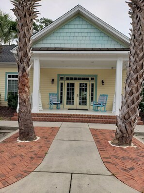 A building with a light blue shingled roof, a porch with two blue chairs, and a brick pathway leading to the entrance.