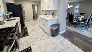 Une cuisine moderne avec des meubles blancs, un sol en marbre et un coin repas comprenant une table et des chaises.