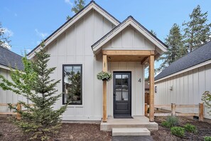 A modern house with a black front door, a wooden porch, and a small garden area.