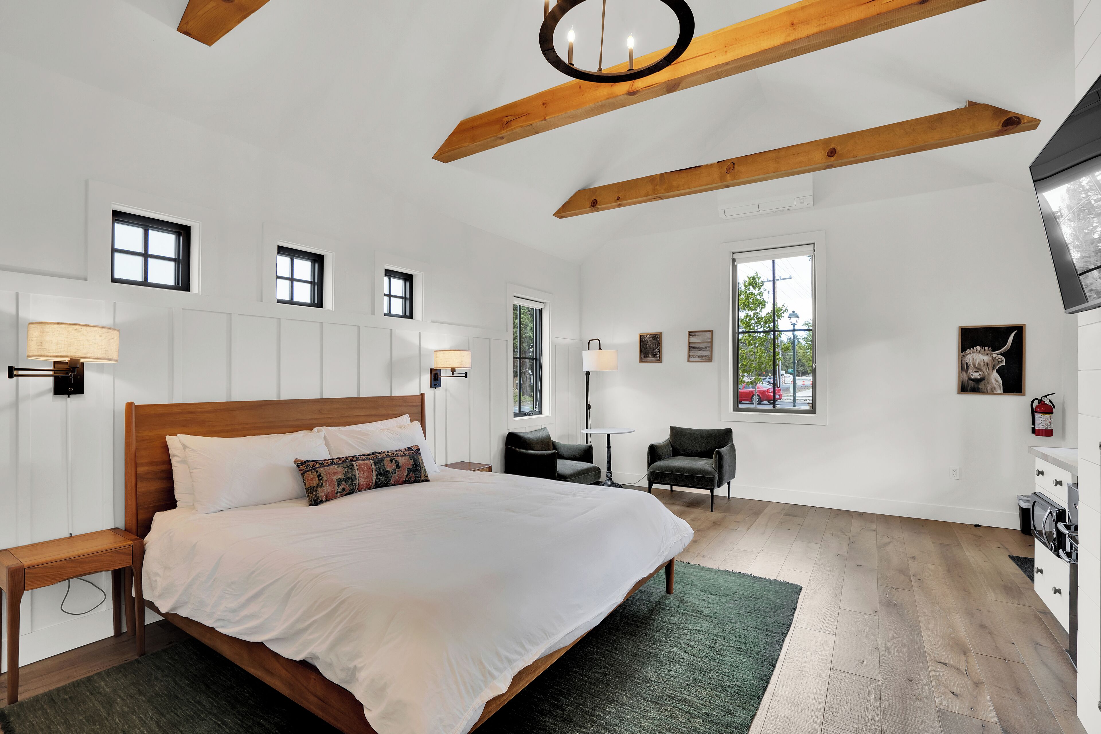 A bedroom with a large bed, wooden beams, a small table, two chairs, a window, and a view of the outside.