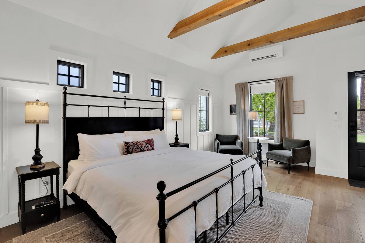 A bedroom with a large bed, two bedside tables with lamps, a chair, and a window with curtains.
