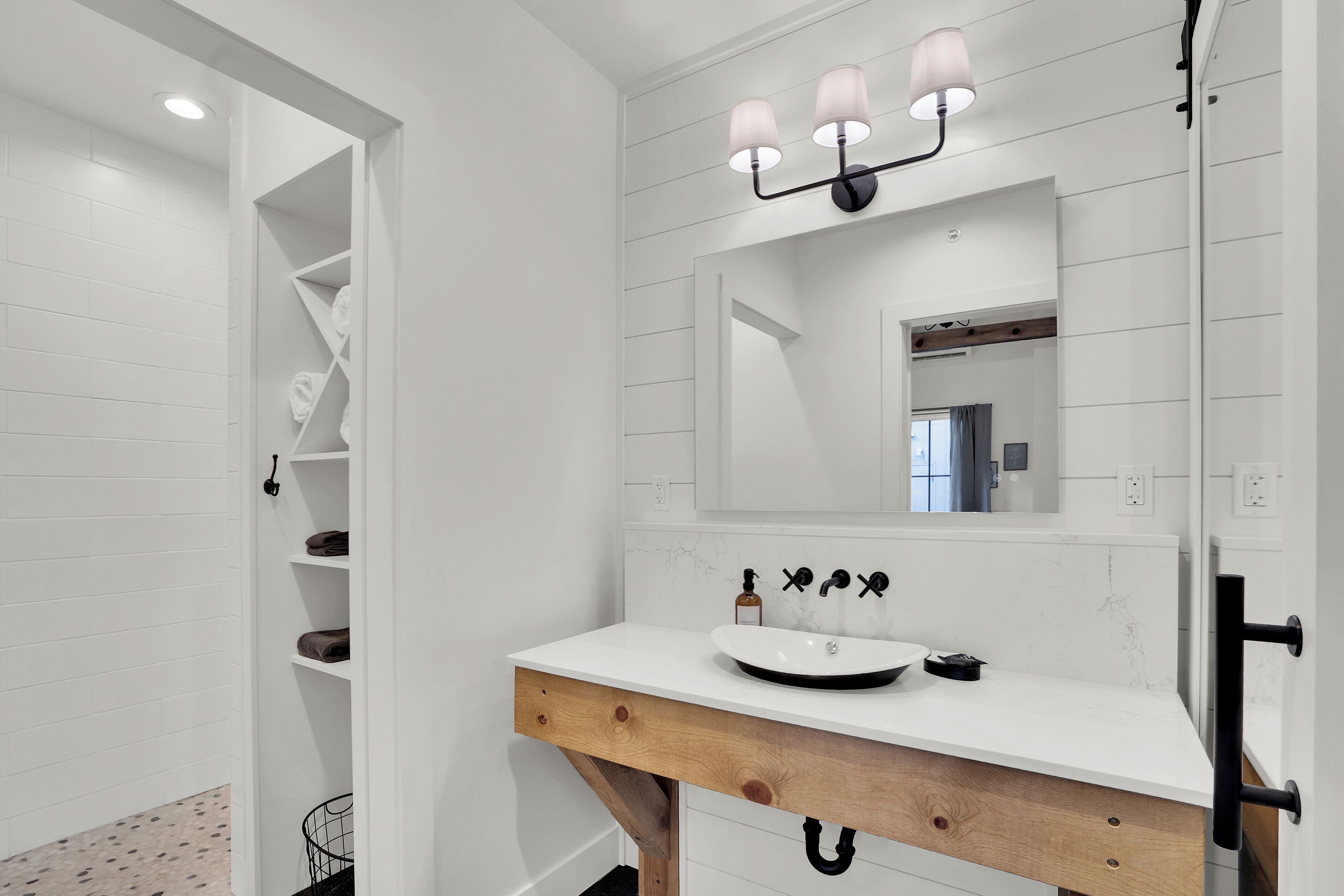 Un baño moderno con tocador blanco, espejo y estante empotrado con toallas.