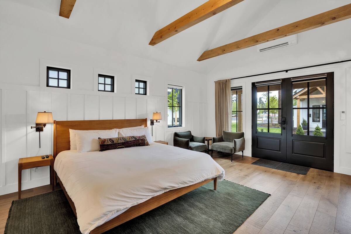 A spacious bedroom with a large bed, two bedside tables, a chair, and a door leading to a balcony.