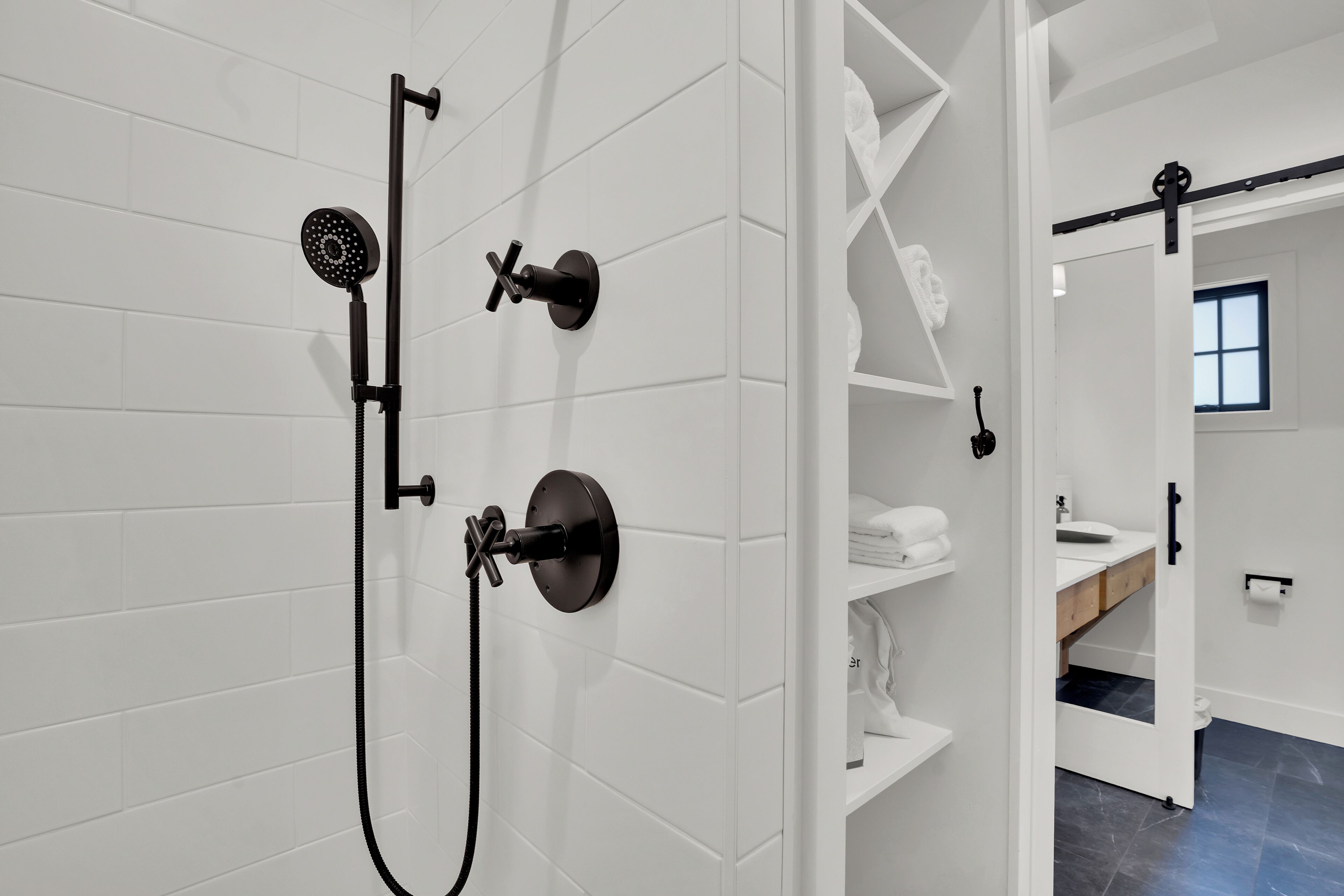 A modern bathroom with white tiled walls, a black showerhead, and a visible toilet area.