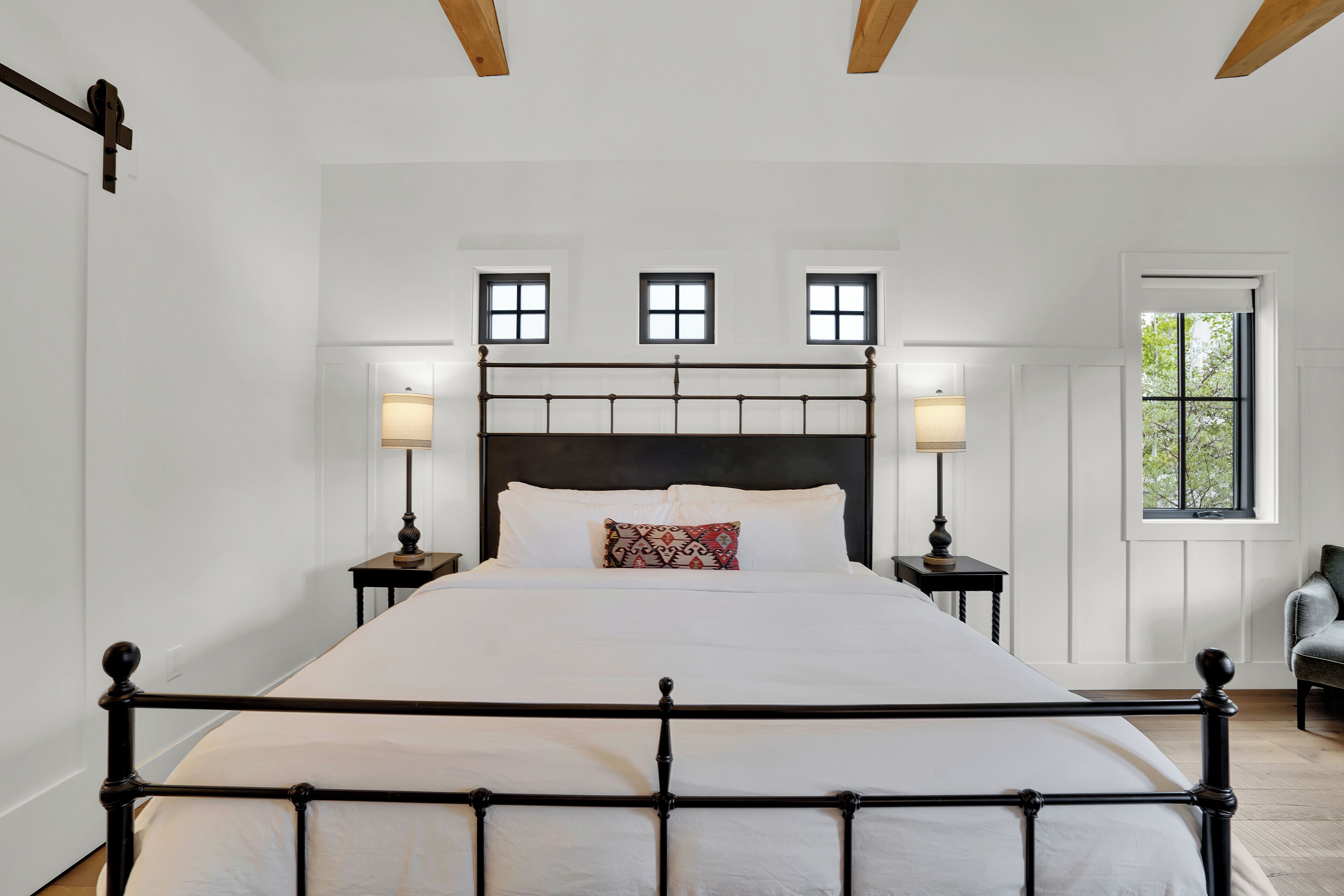 A bedroom with a large bed, two bedside tables with lamps, a window with a view of trees, and a chair.