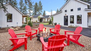 Ein Lagerfeuer mit roten Adirondack-Stühlen vor einem weißen Gebäude mit geneigtem Dach.