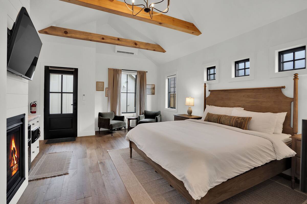 A bedroom with a large bed, a fireplace, a TV, and a desk with chairs.