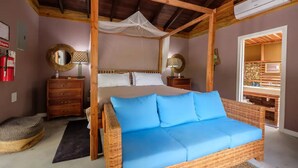 A bedroom with a four-poster bed, a wicker sofa, a wooden nightstand, and a mirror.
