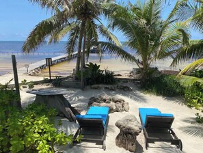 Una playa con sillones de playa y zona de piscina, rodeada de palmeras y rocas.