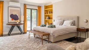 Un dormitorio con una cama grande, un banco, una mesita de noche y vistas al exterior.