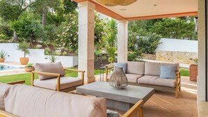 Un patio al aire libre con mobiliario, una piscina y abundante vegetación.