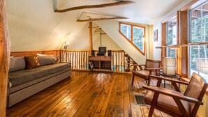 Una habitación acogedora con suelo de madera, un sofá, un escritorio con computadora y ventanas amplias.
