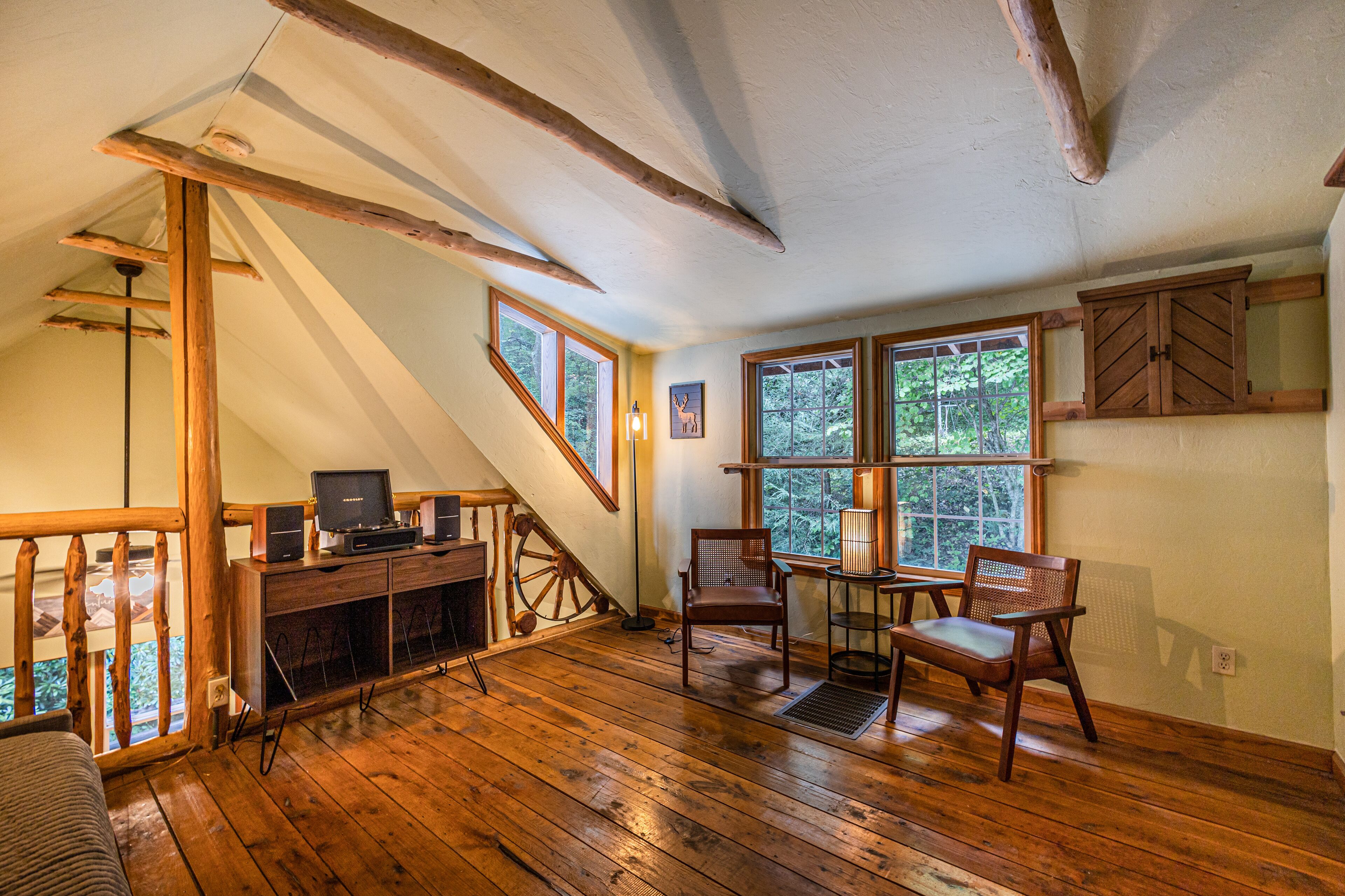 A wooden interior with a loft area, a desk with a computer, and a dining table with chairs.