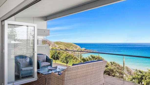 A balcony with a glass door, wicker furniture, and a view of the ocean. - 154 Mitchell Parade - Ocean views from every room (Mollymook Beach)
