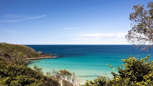 A coastal landscape with clear turquoise waters, a rocky shoreline, and dense greenery. - 154 Mitchell Parade - Ocean views from every room (Mollymook Beach)