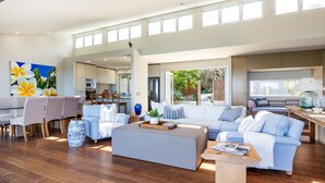 A spacious living area with a dining set, a sofa set, and a kitchen visible through an open door. - 154 Mitchell Parade - Ocean views from every room (Mollymook Beach)