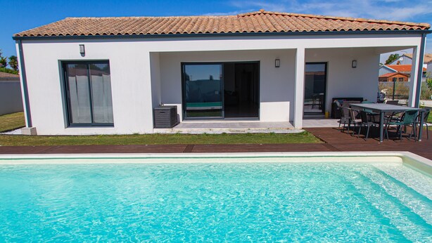 Ein modernes Haus mit Swimmingpool, einer Terrasse und Gartenmöbeln sowie einem Ziegeldach.