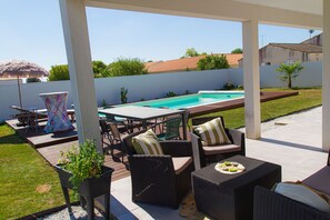 Une terrasse extérieure aménagée avec des meubles en osier, une piscine et une table dressée pour les repas.