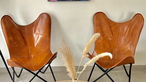 Ein Zimmer mit zwei braunen Ledersesseln, einem runden Holztisch und einer Vase mit Pampasgras. Ein farbenfrohes Gemälde hängt an der Wand.