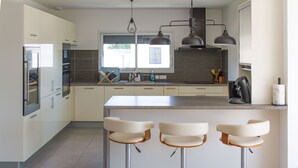 Eine moderne Küche mit weißen Schränken, einer zentralen Kochinsel mit Barhocker und Pendelleuchten.