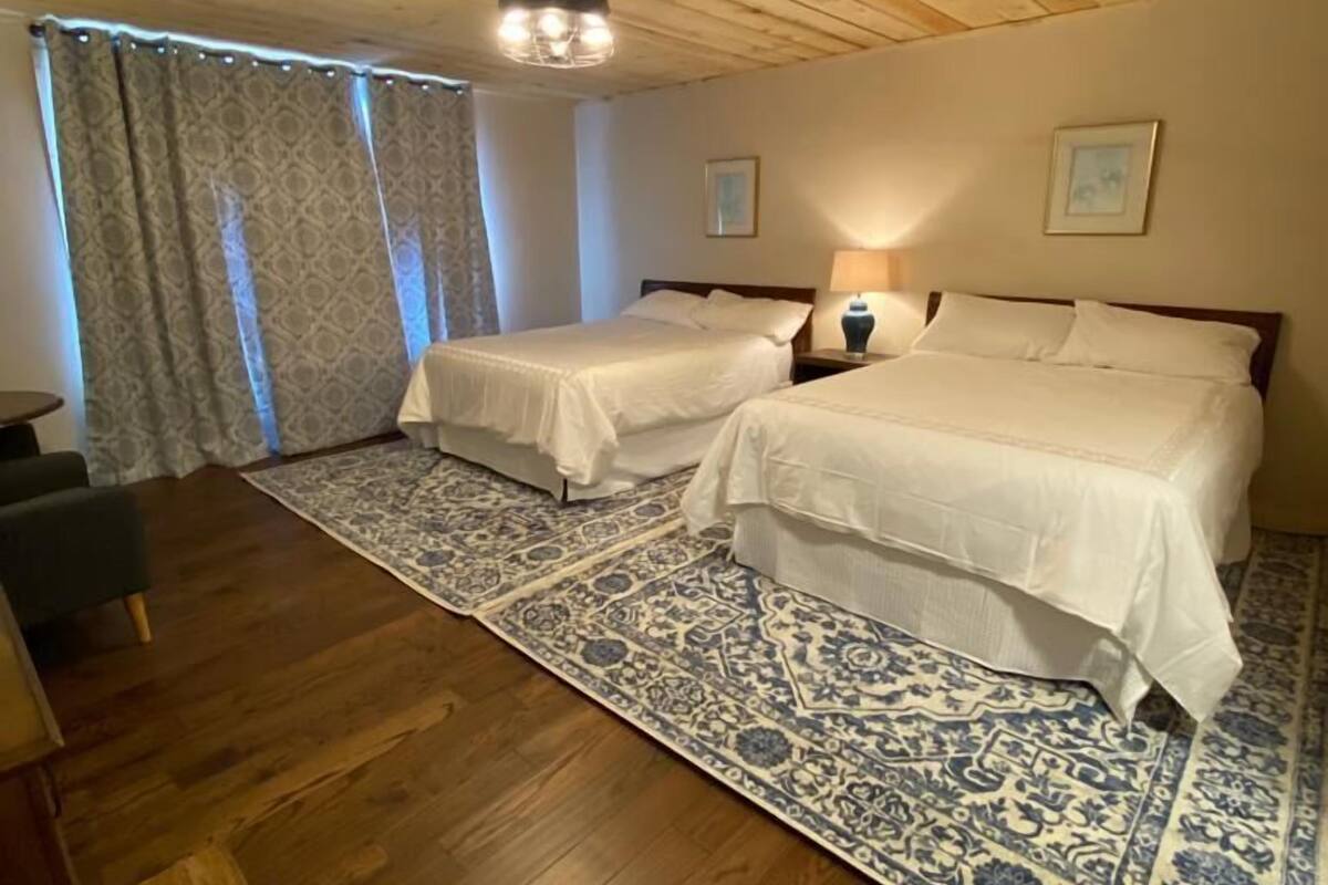 Una habitación con dos camas, techo de madera, alfombra estampada y una pequeña mesa.