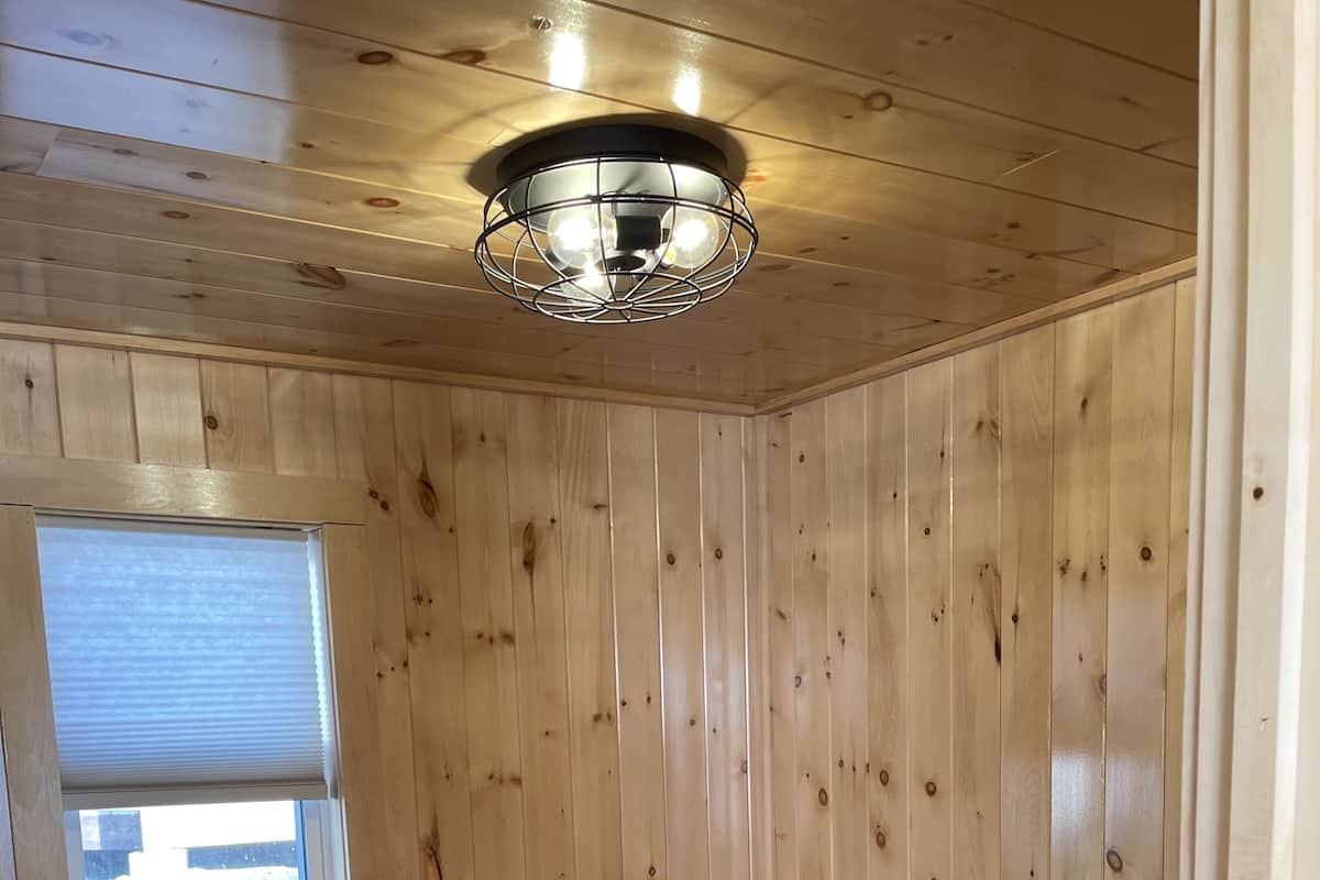 Una habitación con paneles de madera, una cama, una ventana y una lámpara en el techo.