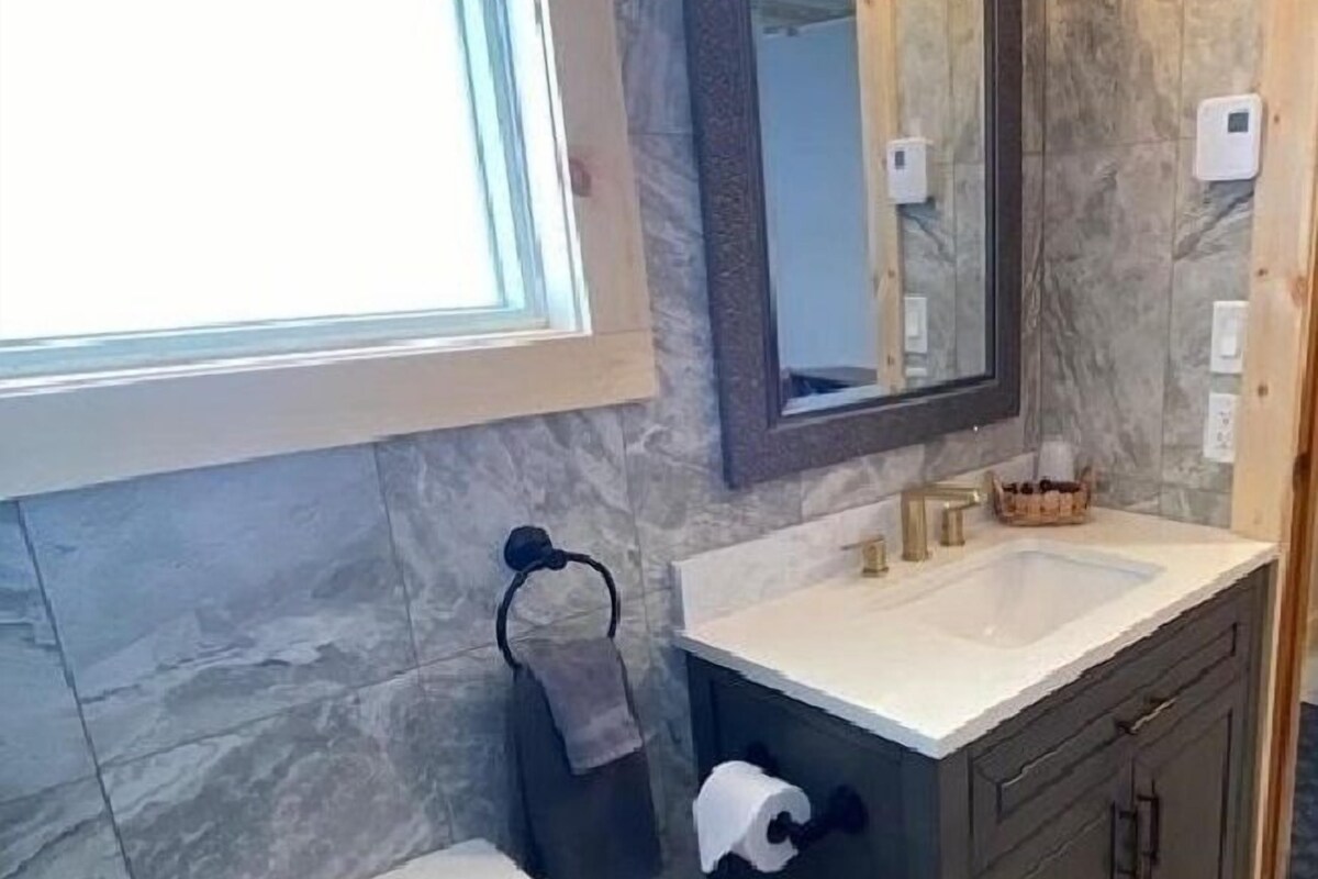 Un baño con inodoro, lavamanos, espejo y perchero para toallas.
