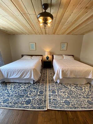 A room with two beds, a patterned rug, a ceiling fan, and framed pictures on the wall.
