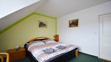 A bedroom with a sloped ceiling, a bed with a patterned bedspread, two framed pictures on the wall, a bedside table with a lamp, and a chair.