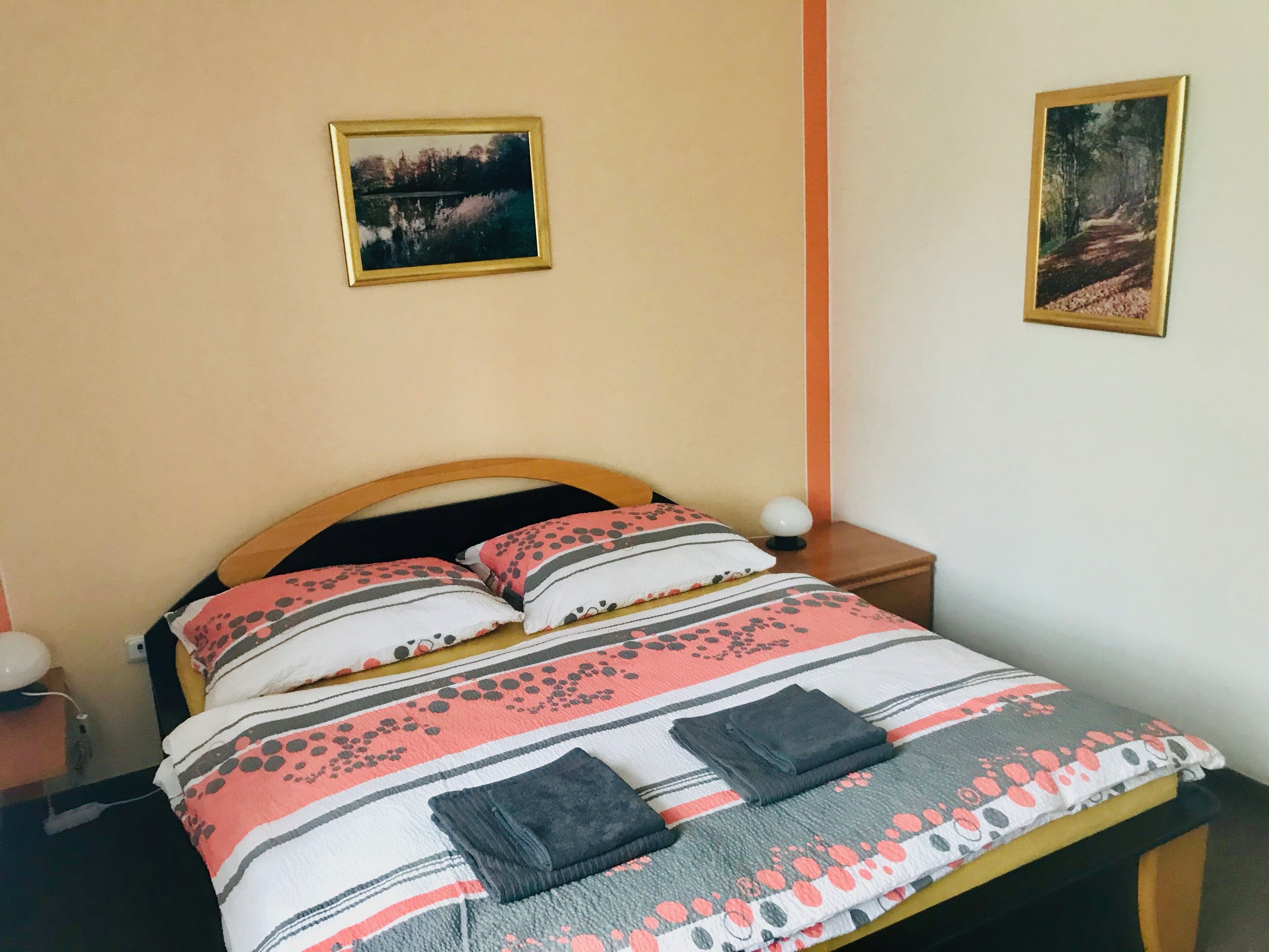 A neatly made bed with patterned bedding, two bedside tables with lamps, and two framed pictures on the walls.