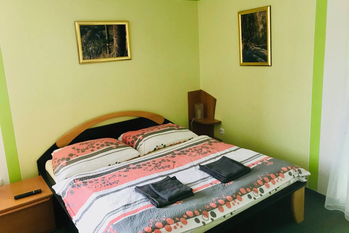 A bedroom with a bed, two framed pictures on the wall, a bedside table, and a nightstand.