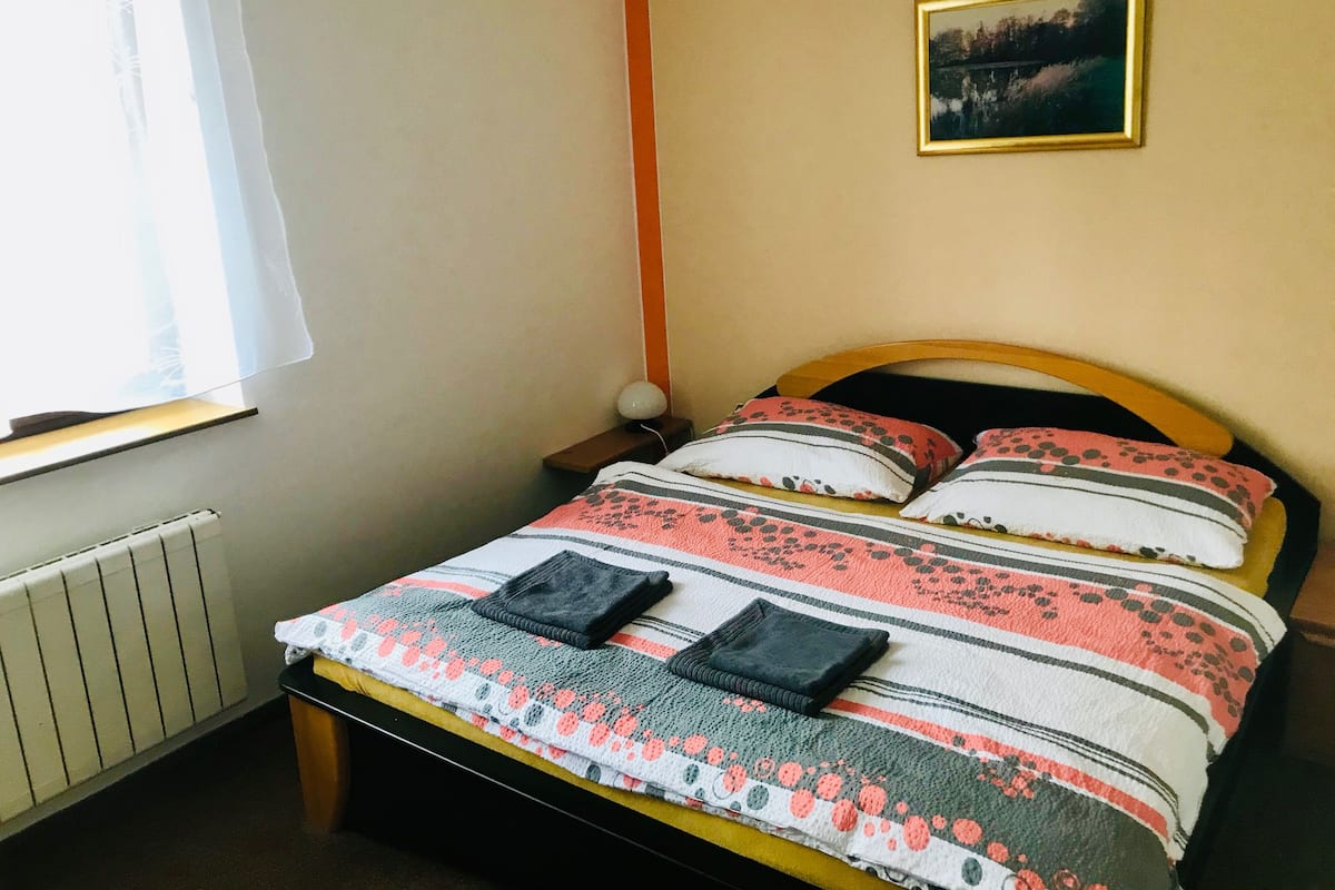 A neatly made bed with a floral-patterned duvet, pillows, and a small bedside table with a lamp.
