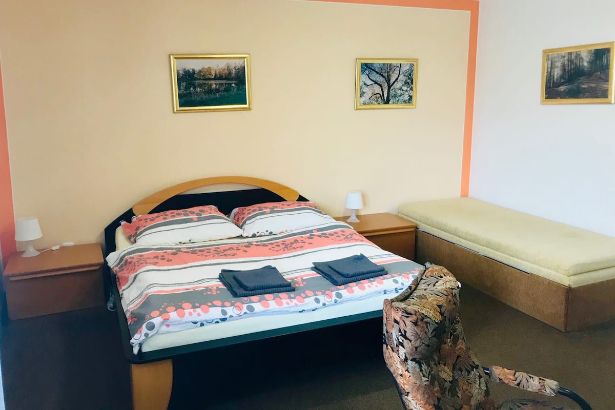 A bedroom with a bed, a nightstand, a chair, and two wall-mounted pictures.