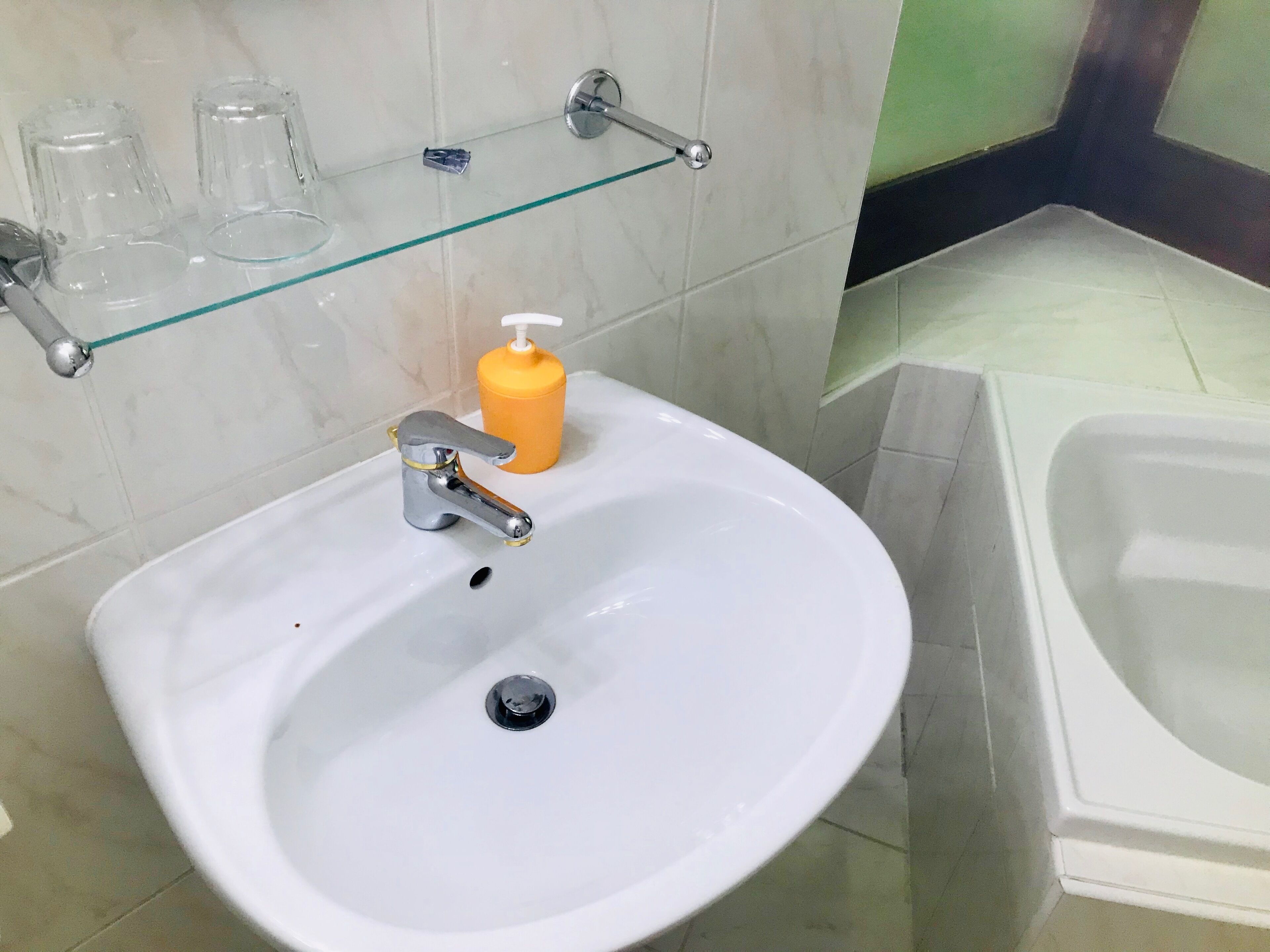 A bathroom with a white sink, a glass shelf with toiletries, and a bathtub.