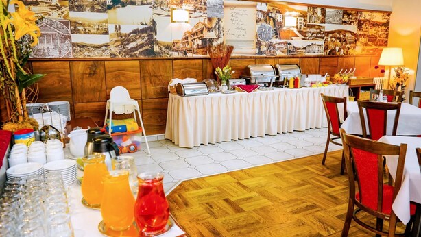 A buffet setup with a variety of food items and drinks, a wooden wall with historical photos, and a wooden floor. - Penzion JANY (Luhacovice)