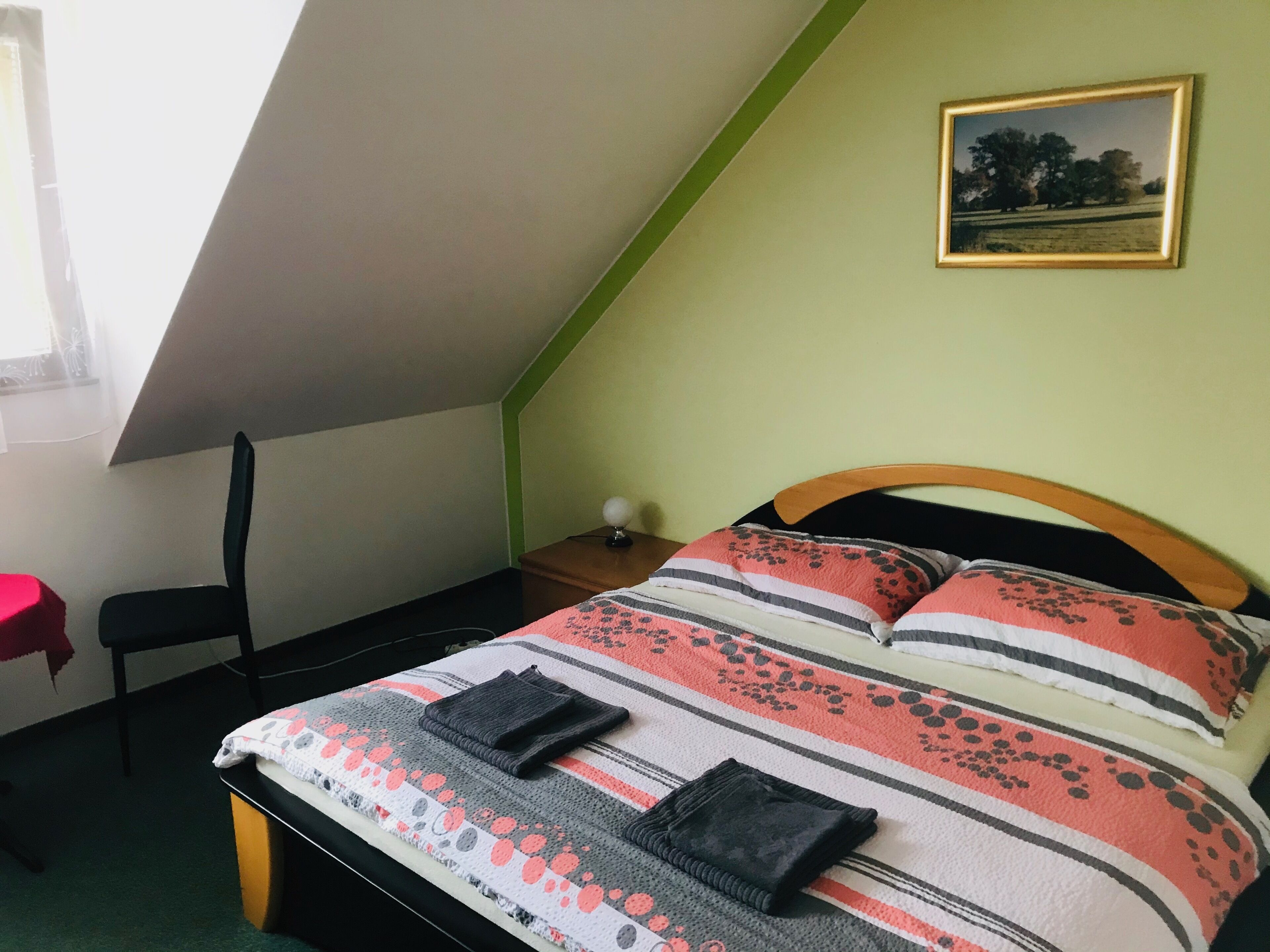 A bedroom with a sloped ceiling, a bed with striped bedding, a nightstand, a chair, and a framed picture on the wall.