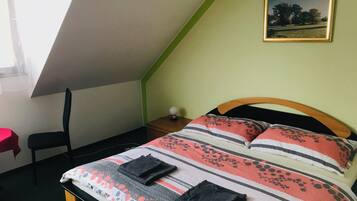 A bedroom with a sloped ceiling, a bed with striped bedding, a nightstand, a chair, and a framed picture on the wall.