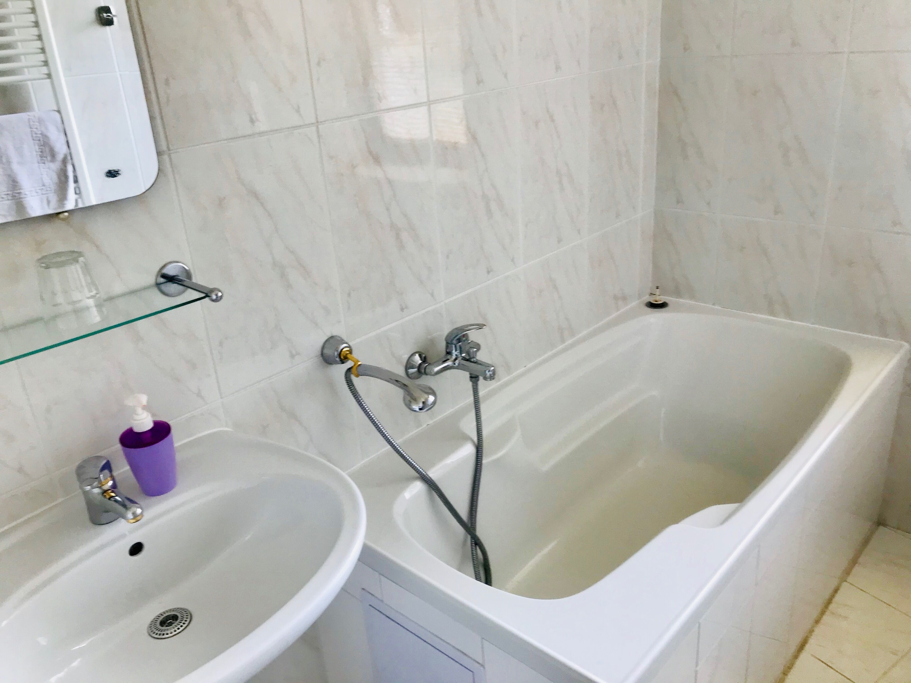 A bathroom with a white bathtub, a sink, and a glass shelf with toiletries.