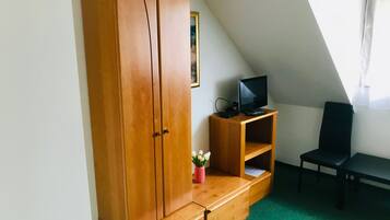 A room with a wooden wardrobe, a small wooden TV stand with a TV, a chair, and a green carpet.
