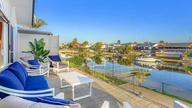 A deck with blue and white furniture overlooking a calm water body with boats, surrounded by residential buildings.