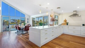 A spacious kitchen with a large island, white cabinetry, and a view through large windows.