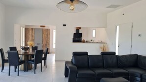 A modern living room with a black leather sofa, a dining area with a wooden table and chairs, and a kitchen area with a black countertop and appliances. - Villa 8pers with view and exceptional swimming pool (Bargemon)