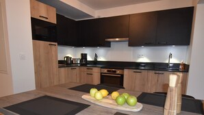 A modern kitchen with wooden cabinets, a black countertop, and a central island with fruits. - L'Étendard appartement 5 (Vaujany)